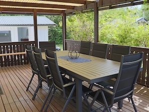Un patio al aire libre con una mesa y sillas de madera, rodeado por una terraza de madera y una barandilla de metal.