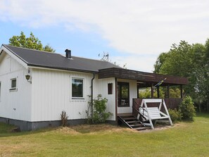 A single-story white building with a dark roof, a porch with a wooden railing, and a small set of stairs leading to the entrance.