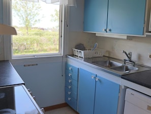 A kitchen with blue cabinets, a stainless steel sink, and a window with a view of greenery.