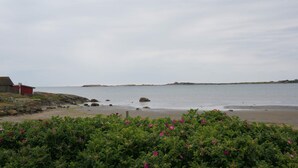 A coastal landscape with a sandy beach, a red building, and a rocky outcrop in the distance. - 4 Star Holiday Home in Traslovslage (Träslövsläge)