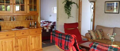 Una sala de estar acogedora con un aparador de madera, un sillón rojo, un sofá y una mesita con un jarrón.