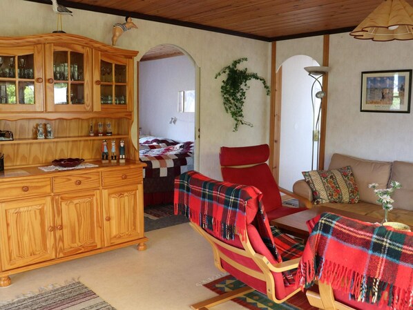 A cozy living room with a wooden cabinet, a red chair, a sofa, and a small table with a vase.