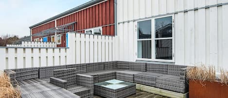 A covered outdoor seating area with wicker furniture and a wooden deck.