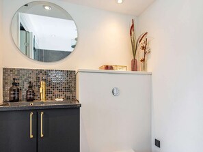 A bathroom with a dark countertop, a round mirror, and a white wall. - Welcoming Holiday Home in Ebeltoft (Ebeltoft)