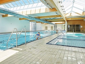 An indoor swimming pool with clear water, metal ladders, and a tiled floor.