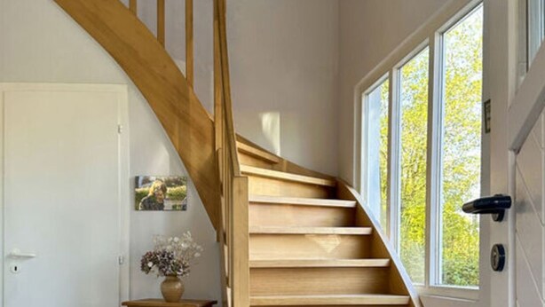 A wooden staircase leading to a second floor, a door, a small cabinet with a vase, and a window with a view of trees. - Holiday Apartment Sauer Large (Varel)