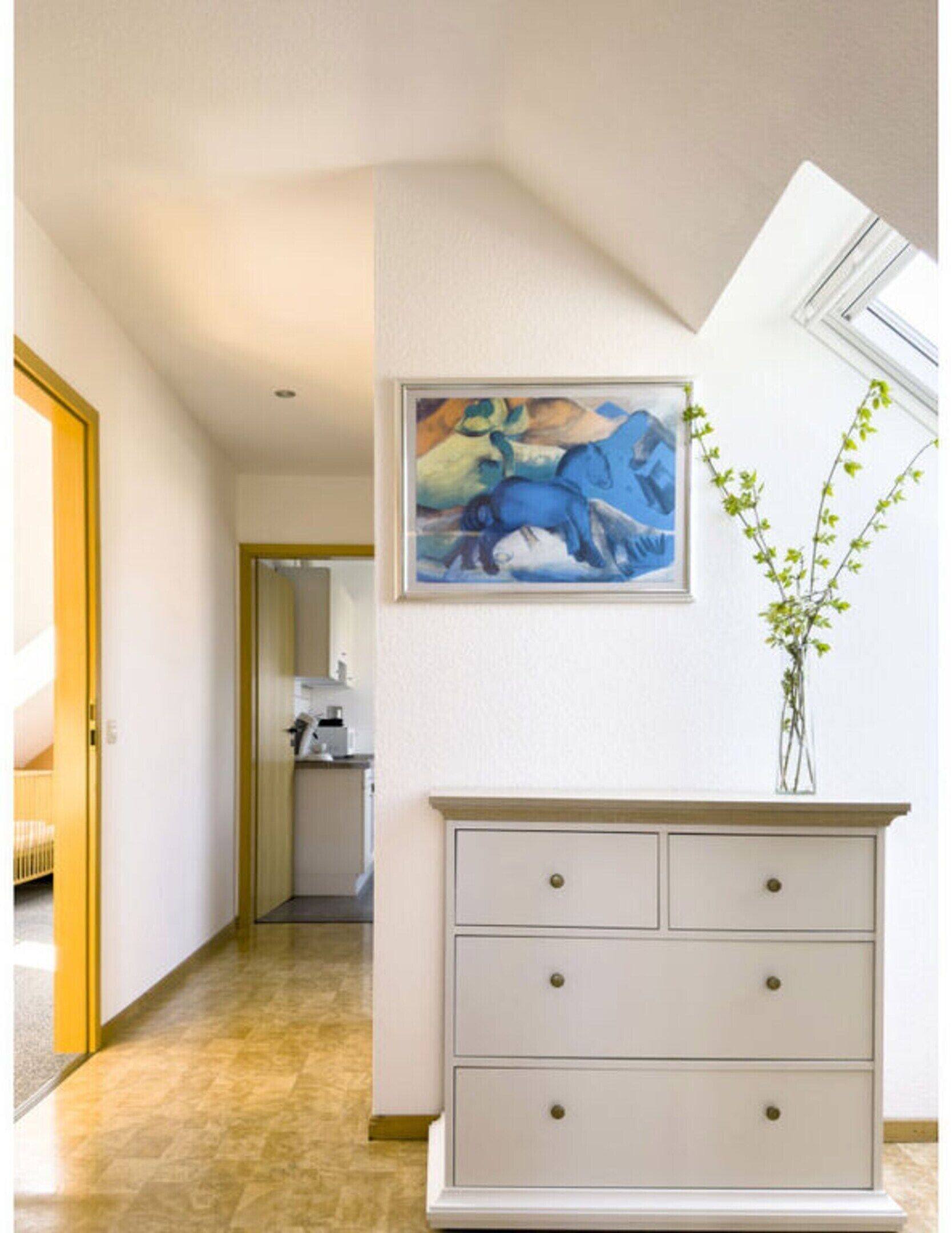 A hallway with a white dresser, a painting of a horse, and a vase with green plants.