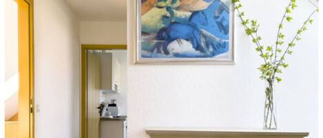 A hallway with a white dresser, a painting of a horse, and a vase with green plants.