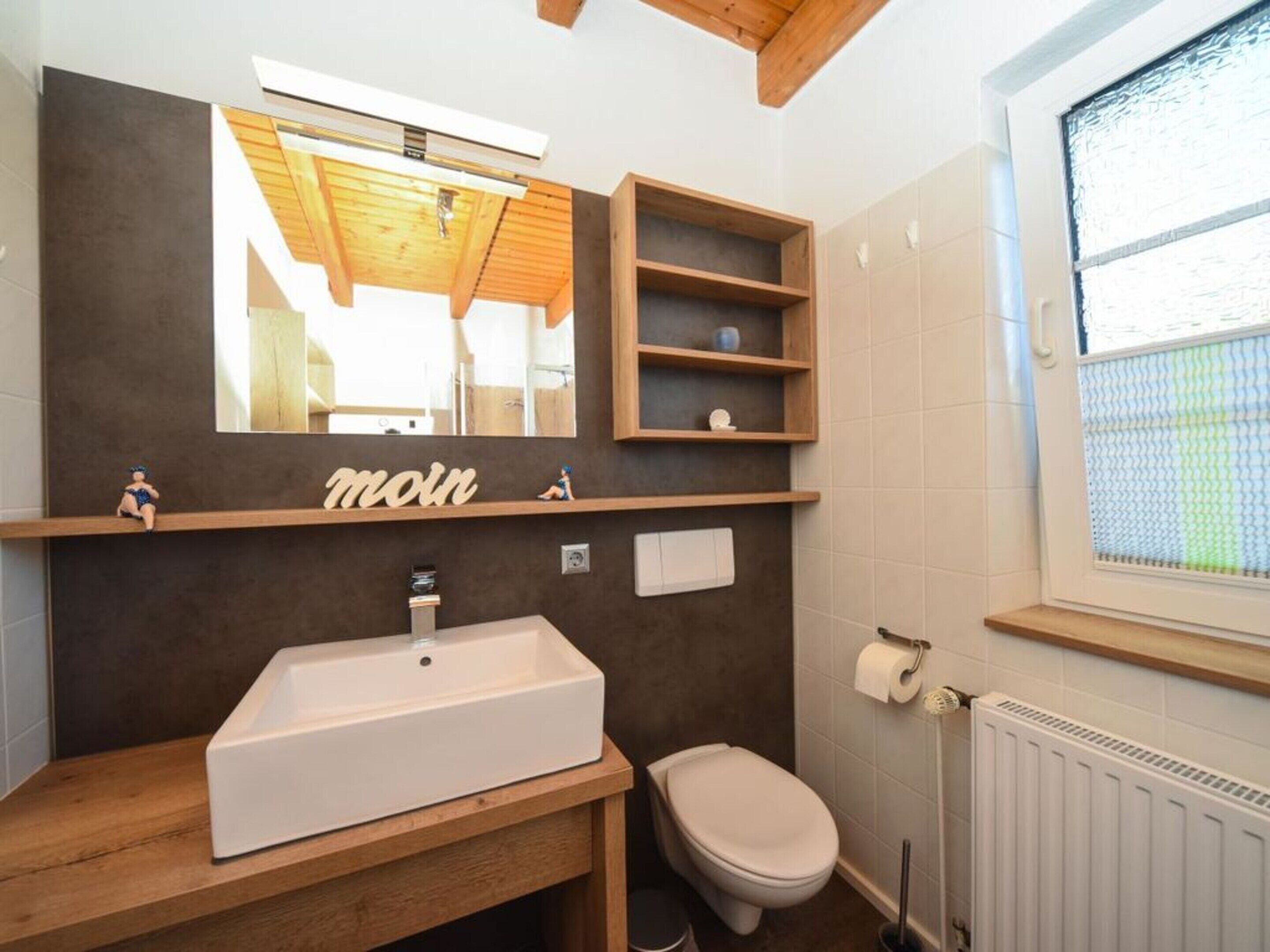 A modern bathroom with a wooden vanity, a large mirror, and built-in shelves.