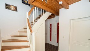 A wooden staircase with white railings leading to a room with a wooden ceiling and a door with red accents. - Holiday Home Nispel 2 (Dornum)