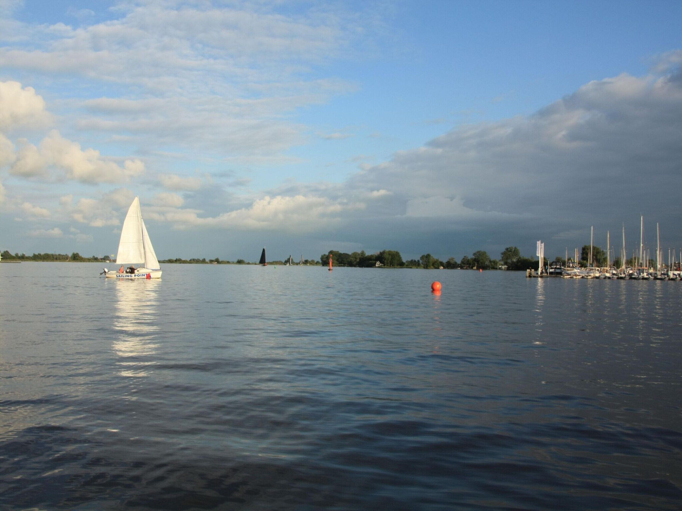 A calm body of water with a sailboat and several other boats docked in the background.