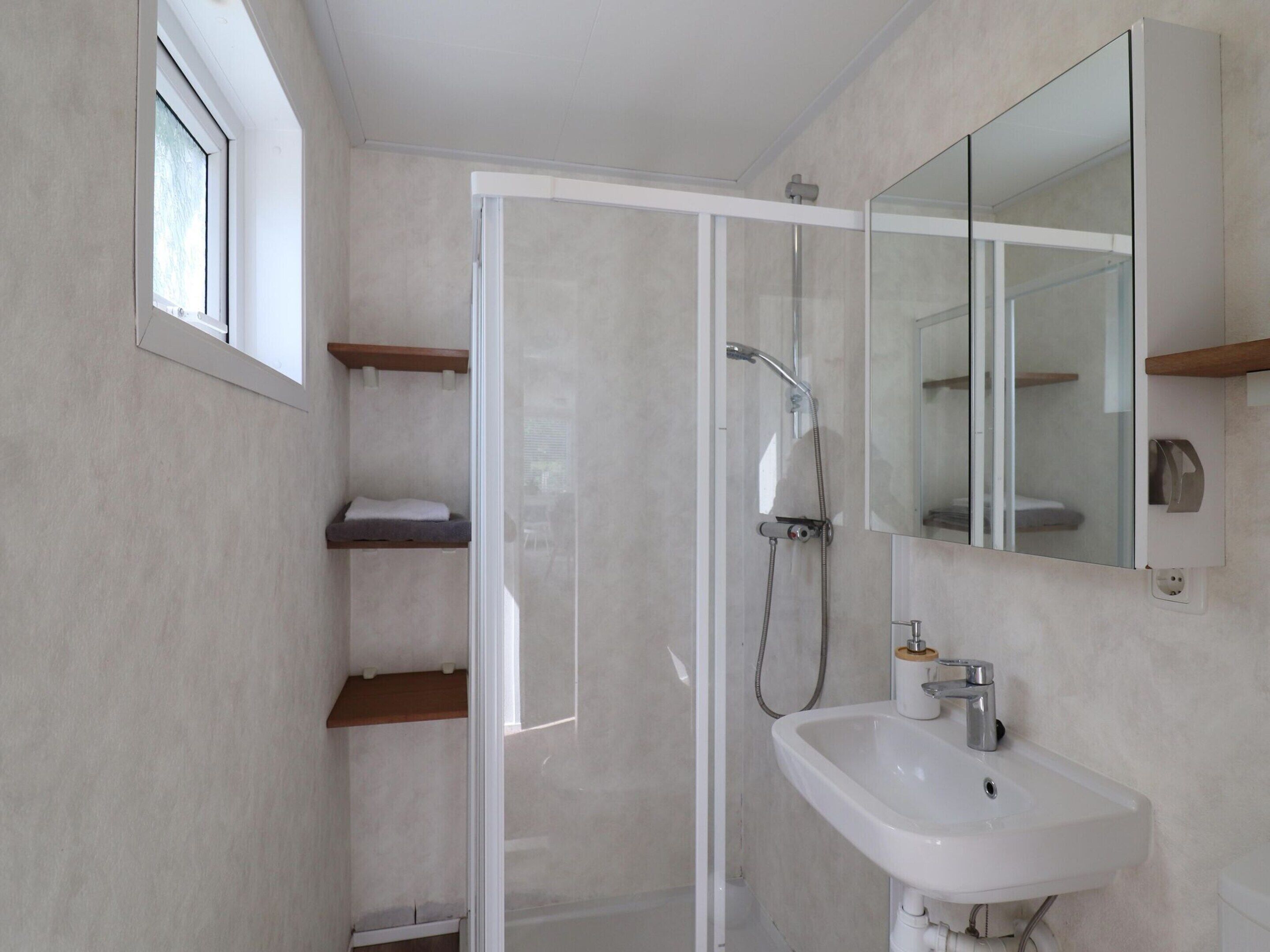 Une salle de bain moderne avec une douche à parois de verre, un lavabo blanc et des étagères intégrées.
