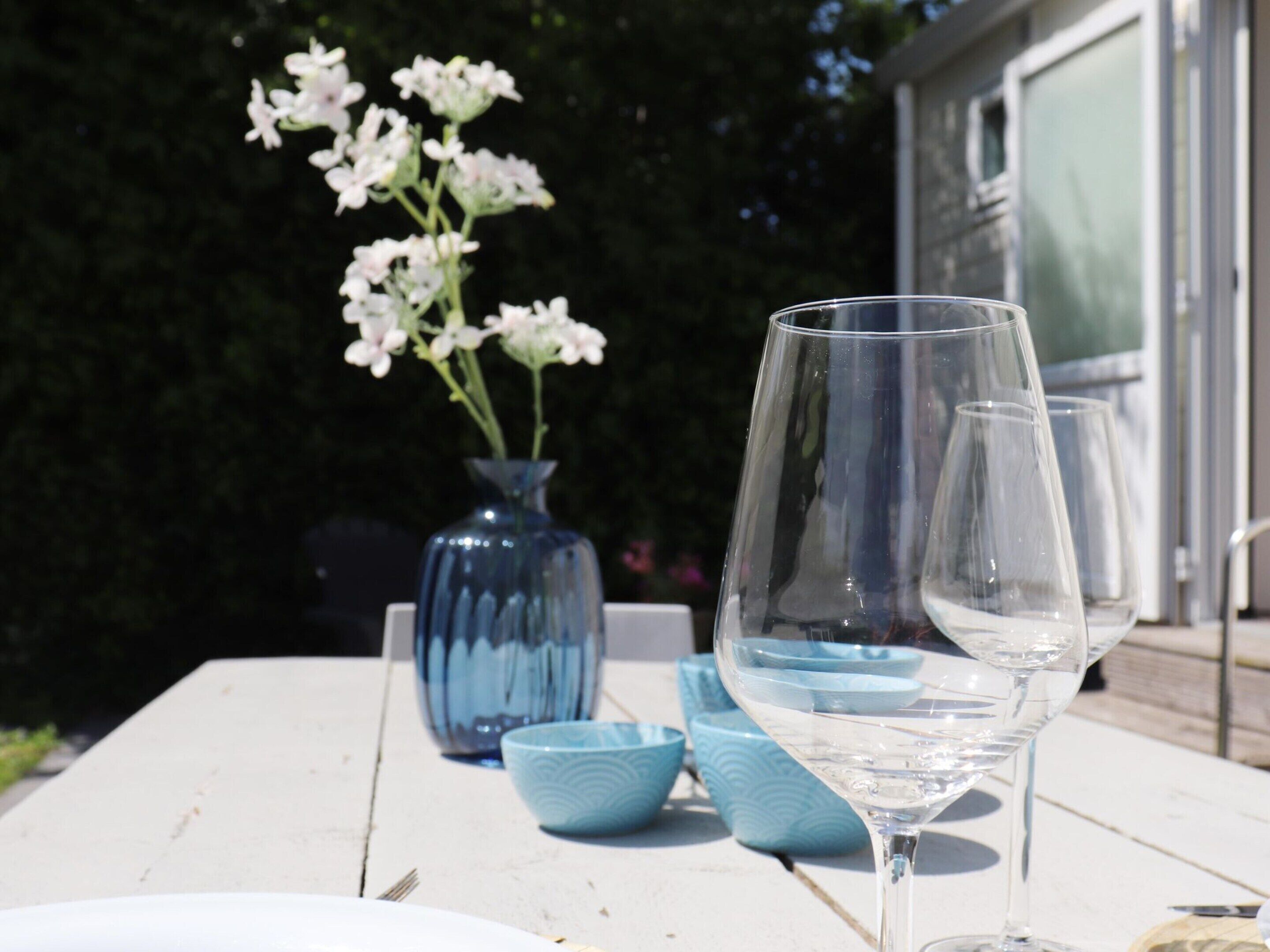 Et bord med et drikkeglas, en vase med blomster og blå skåle.