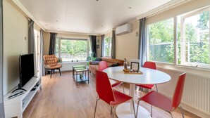 A modern living room with a sofa, red chairs, a TV, and a dining table. - Serene Forest Stay With Comfort (Putte)