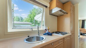 A compact kitchen with a window, stainless steel sink, wooden cabinets, and a gas stove. - Serene Forest Stay With Comfort (Putte)