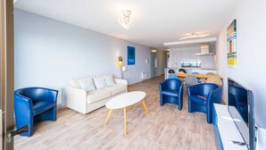 A modern living room with a white sofa, blue chairs, a white coffee table, and a kitchen in the background. - Seaside Stay Middelkerke (Middelkerke)