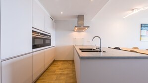 A modern kitchen with white cabinetry, a central island with a sink, and a built-in oven. - Seaside Stay Middelkerke (Middelkerke)
