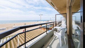 A balcony with a view of the beach, white plastic chairs, and a wooden deck. - Seaside Stay Middelkerke (Middelkerke)