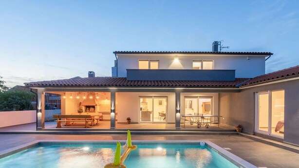Una casa moderna de dos pisos con piscina, zona de comedor al aire libre y un porche cubierto.