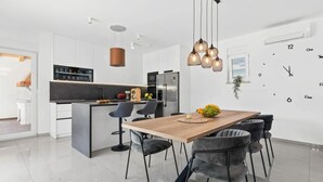 Cocina moderna con armarios blancos, una isla central y un comedor con mesa y sillas de madera.