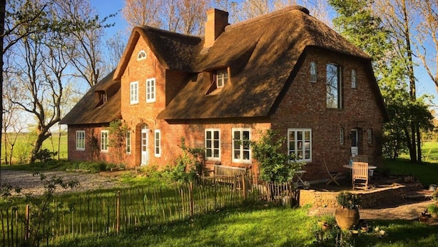 A large brick house with a thatched roof, surrounded by a well-maintained garden and trees. - Warft Simmerdeis 2 Comfortable Holiday Residence (Oldenswort)