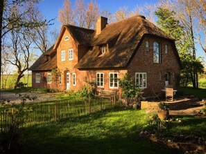 A large brick house with a thatched roof, surrounded by a well-maintained garden and trees. - Warft Simmerdeis 2 Comfortable Holiday Residence (Oldenswort)