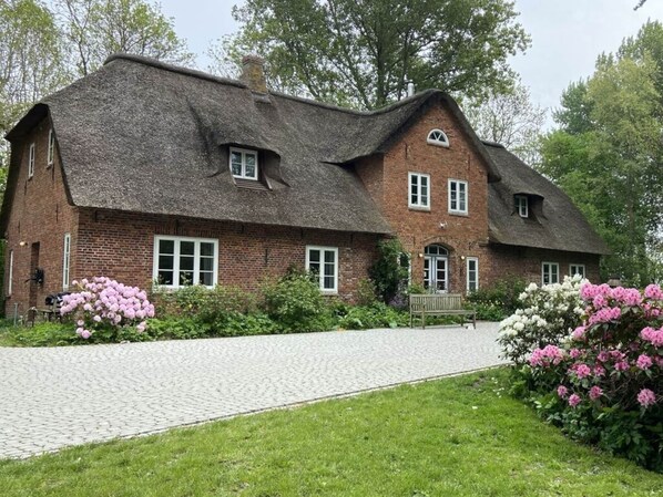 A traditional brick house with a steeply pitched thatched roof, a paved driveway, and a bench in the garden. - Warft Simmerdeis 2 Comfortable Holiday Residence (Oldenswort)