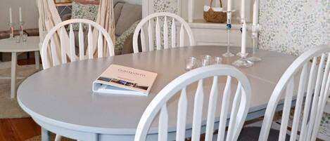 Un comedor con una mesa redonda, sillas blancas y un libro titulado 'Gästspår'.