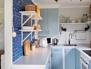 A kitchen with blue cabinets, white countertops, and a microwave. There are shelves with jars and a basket. - 4 Person Holiday Home in Varberg (Varberg)