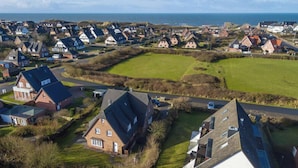 An aerial view of a coastal village with traditional houses, open green spaces, and a clear view of the sea. - Holiday Home Hiirlonhus (Wenningstedt-Braderup)