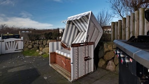 A large, uniquely designed outdoor seating area with a metal frame and striped fabric cover, adjacent to a stone wall and a wooden fence. - Holiday Home Hiirlonhus (Wenningstedt-Braderup)
