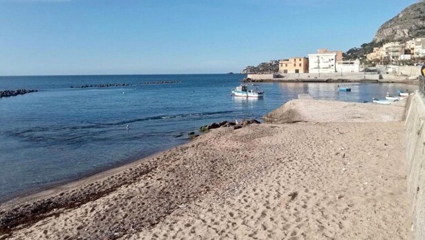 Une plage côtière avec un rivage sablonneux, un petit bateau et des bâtiments en arrière-plan.