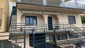 Un immeuble résidentiel de deux étages doté d’un balcon, d’un escalier et d’une entrée fermée par un portail.