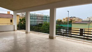 Un balcon spacieux doté d’un sol en béton et de rampes en métal, offrant une vue sur un quartier résidentiel avec des maisons et un terrain de sport.