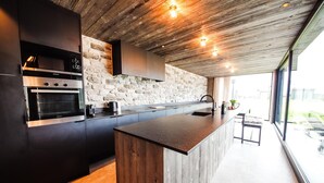 A modern kitchen with a built-in oven, a wooden island, and a stone wall backsplash. - Maison Lodge 5 Modern and Luxuriously Finished Near Somme-leuze (Somme-Leuze)