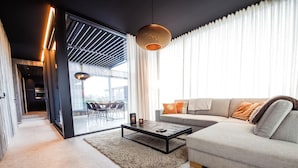 A modern living room with a sofa, coffee table, and a dining area visible through a glass door. - Maison Lodge 5 Modern and Luxuriously Finished Near Somme-leuze (Somme-Leuze)