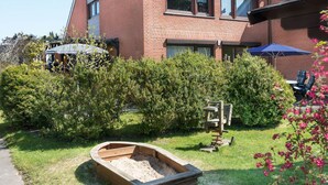 Un immeuble résidentiel à la façade en briques, doté d’un jardin bien entretenu avec un bateau en bois et d’un espace extérieur aménagé pour s’asseoir.