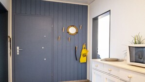 Une pièce avec une porte bleue, un miroir, une petite plante et un sac jaune accroché au mur.