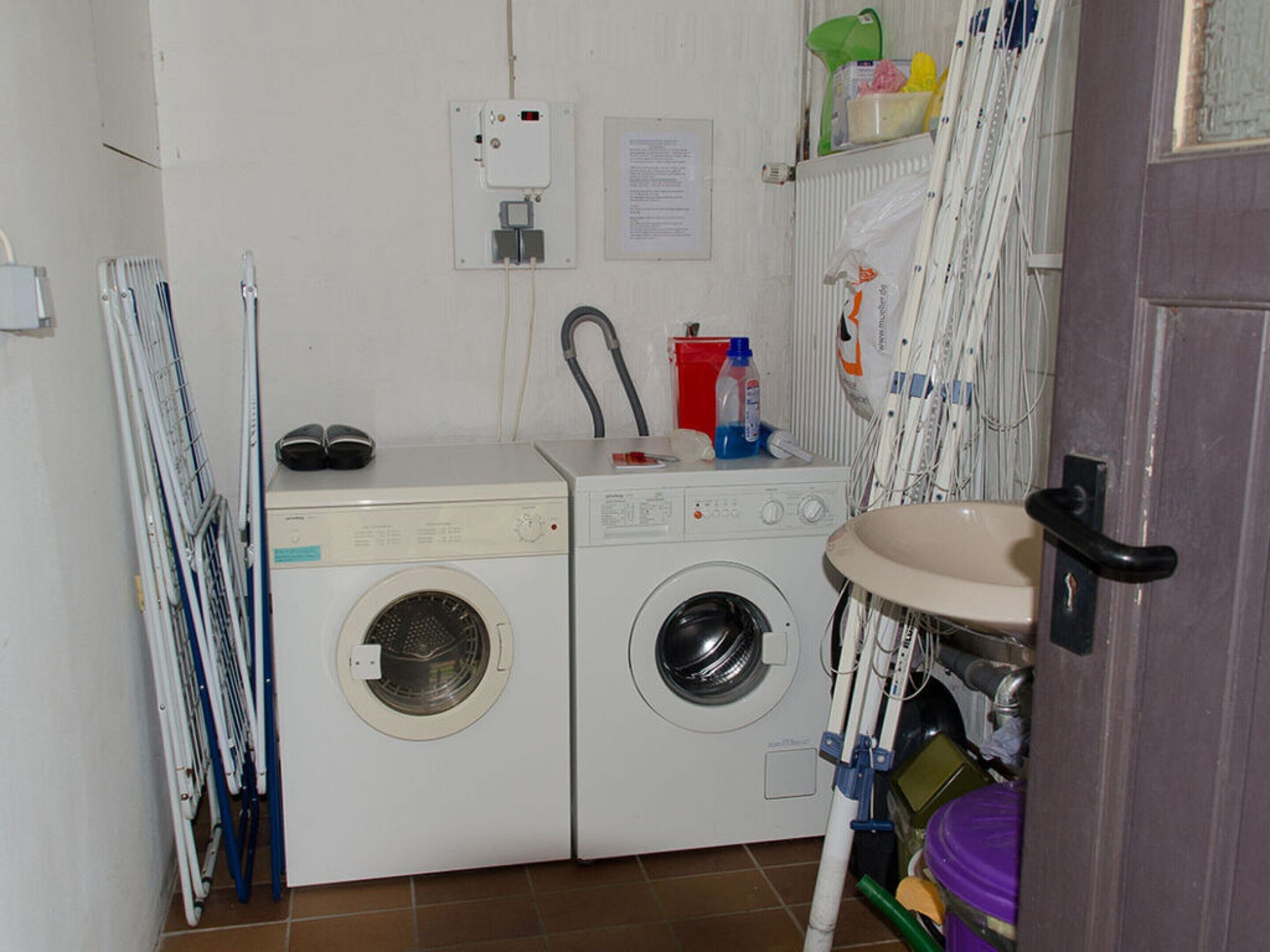 A compact laundry room with two washing machines, a sink, and a drying rack.