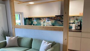 A room with a green sofa, wooden beams, a kitchen area with a coffee machine, and a painting on the wall. - Holiday Home Chalet on the Castle Hill (Brotterode-Trusetal)