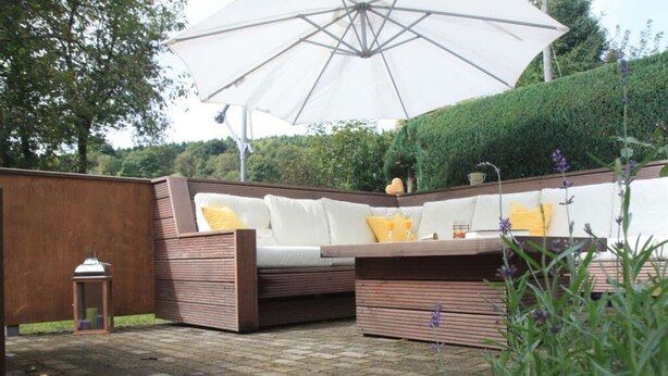 An outdoor seating area with a wooden bench and a white sofa, an umbrella, and a lantern. - Holiday Home Chalet on the Castle Hill (Brotterode-Trusetal)
