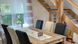 A dining area with a wooden table and chairs, a window with curtains, and a staircase with wooden beams. - Holiday Home Chalet on the Castle Hill (Brotterode-Trusetal)