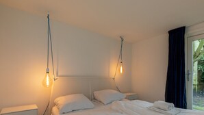 A hotel room with two beds, white bedding, bedside tables, and hanging light bulbs. - Beautiful Bungalow With Garden (Biggekerke)