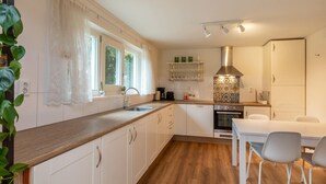 A modern kitchen with white cabinets, a wooden countertop, a built-in oven, and a dining area with a table and chairs. - Beautiful Bungalow With Garden (Biggekerke)