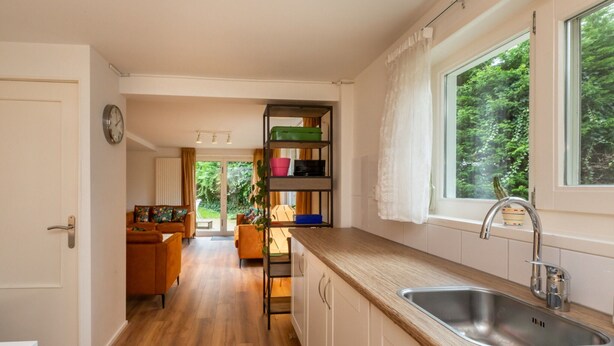 A modern kitchen with wooden flooring, a built-in sink, and a window overlooking greenery. - Beautiful Bungalow With Garden (Biggekerke)