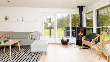 A modern living room with a sofa, a table, a fireplace, and a view of the outdoors.