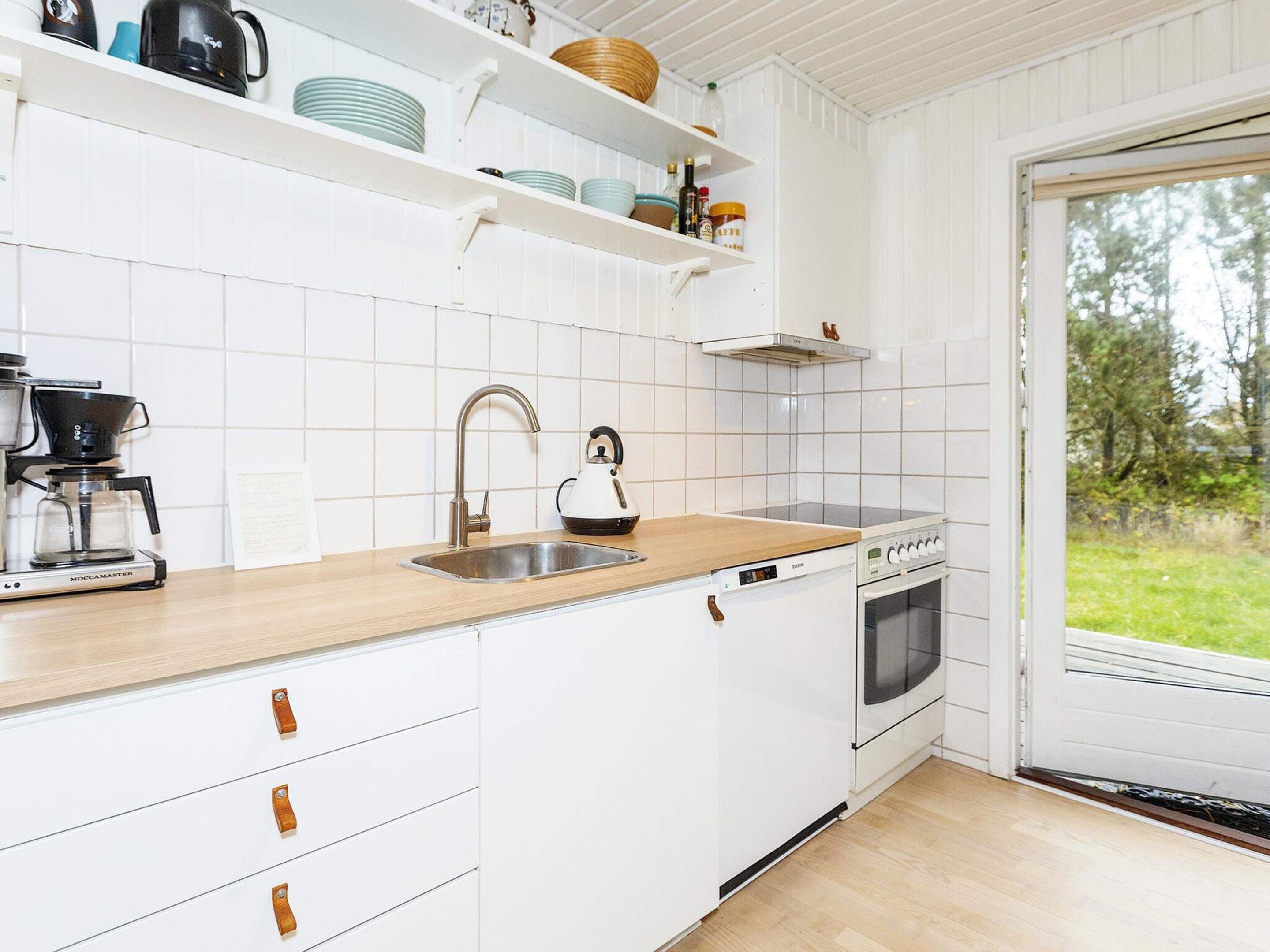 A kitchen with white cabinets, a coffee maker, a kettle, a stove, and a sink.