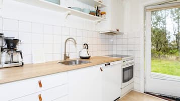 A kitchen with white cabinets, a coffee maker, a kettle, a stove, and a sink.