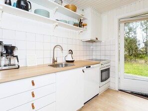 A kitchen with white cabinets, a coffee maker, a kettle, a stove, and a sink.