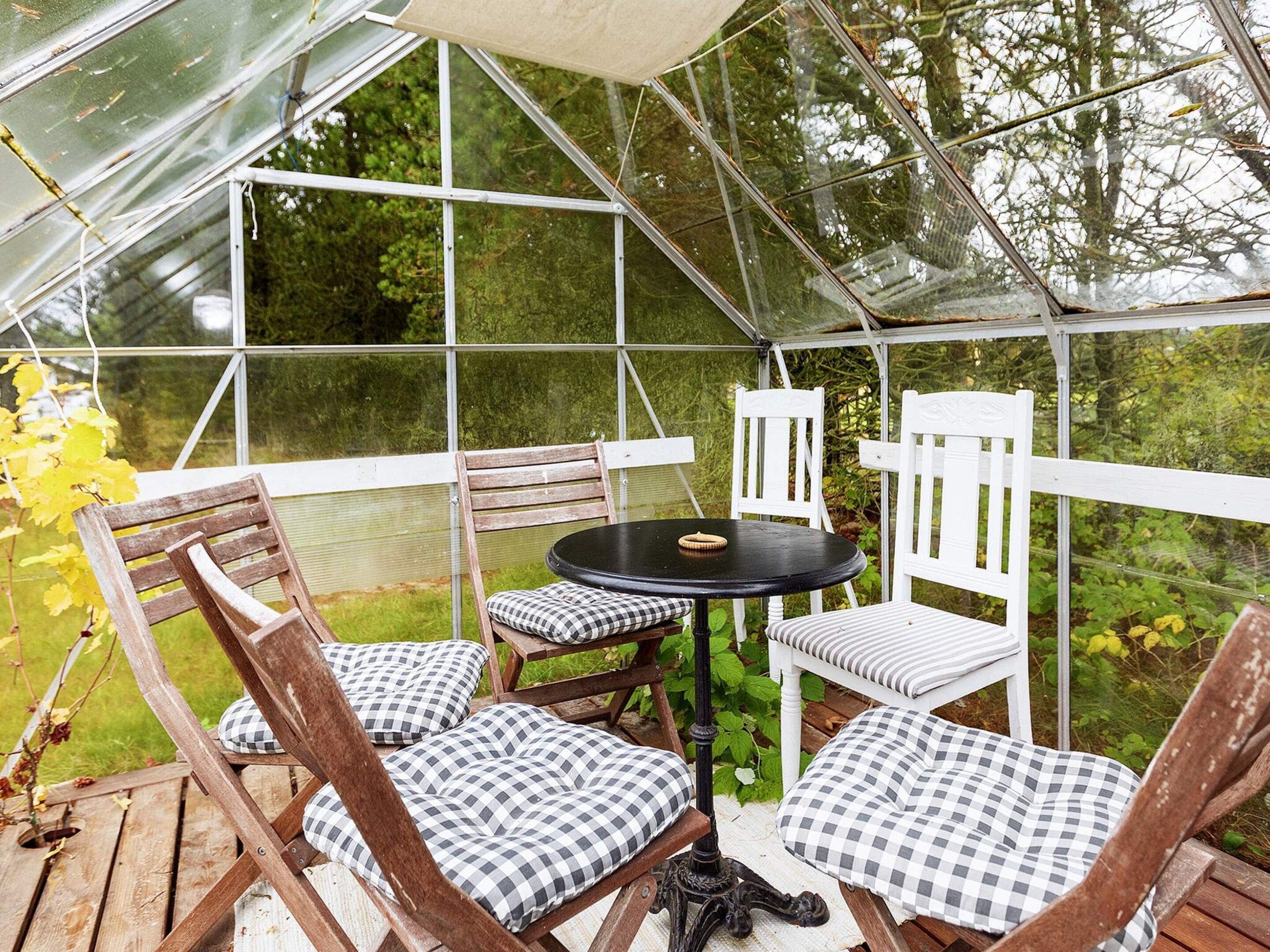 A greenhouse with a table and chairs, surrounded by greenery.
